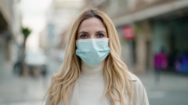 Sokakta tıbbi maske takan genç sarışın kadın.