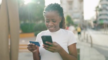 African american woman using smartphone and credit card at park