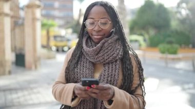 African woman smiling using smartphone at street