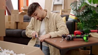 Genç Arap adam yeni evinde tornavida kullanarak masayı onarıyor.