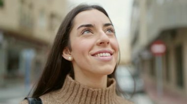 Young beautiful hispanic woman smiling confident looking to the sky at street