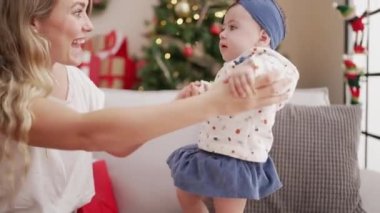 Kadın ve bebek evdeki Noel ağacının yanında kanepede duruyorlar.