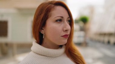 Sokakta ciddi bir ifadeyle duran genç kızıl saçlı kadın.