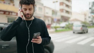 Genç Arap adam kendinden emin bir şekilde gülerek sokakta müzik dinliyor.