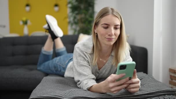 Young Blonde Woman Using Smartphone Lying Sofa Home — 图库视频影像