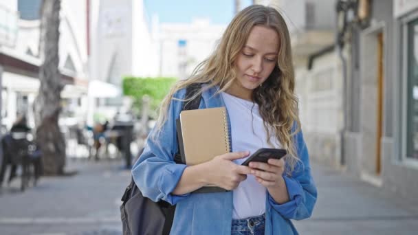 Joven Estudiante Rubia Sosteniendo Libros Usando Smartphone Calle — Vídeo de stock