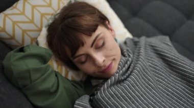 Young caucasian woman sleeping on the sofa covered with blanket at home