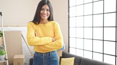 Genç, güzel İspanyol bir kadın, kendine güvenen bir şekilde koltukta oturuyor ve yeni evinde kollarını kavuşturup el kol hareketi yapıyor.