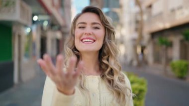 Genç sarışın kadın gülümsüyor. Kendinden emin. Sokakta jest yapıyor.