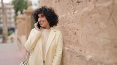 Gülümseyen genç bir kadın caddedeki akıllı telefondan konuşuyor.