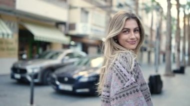 Genç sarışın kadın gülümsüyor. Kendine güveniyor. Sokakta kendine dönüyor.