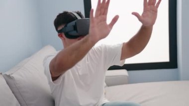 Evde sanal gerçeklik gözlüğü kullanarak video oyunu oynayan İspanyol genç adam.
