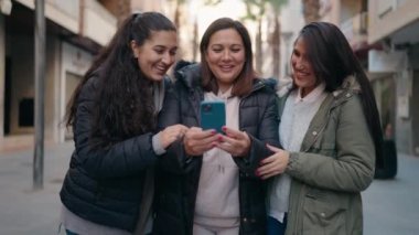 Mother and daughters smiling confident using smartphone at street