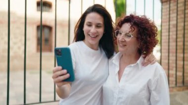 İki kadın anne ve kız birbirlerine sarılıyorlar ve sokakta video görüşmesi yapıyorlar.
