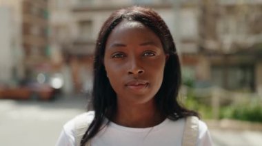 Genç Afrikalı Amerikalı kadın gülümsüyor. Kendine güveni tam. Sokakta kollarını kavuşturmuş duruyor.