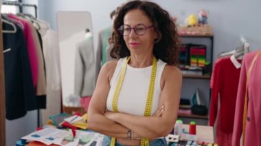 Middle age woman tailor smiling confident standing with arms crossed gesture at clothing factory