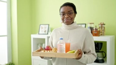 Afro-Amerikalı kadın yemek odasında kahvaltı tepsisi tutarken kendine güveniyor.