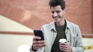 Young hispanic man talking on smartphone drinking coffee at street