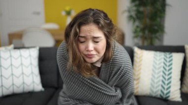 Young beautiful hispanic woman covering with blanket for cold at home