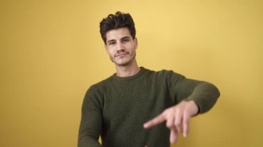 Young hispanic man smiling confident doing photo gesture with hands over isolated yellow background