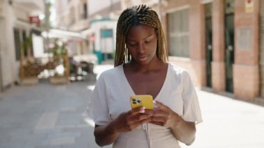 Afro-Amerikalı kadın sokakta akıllı telefon kullanarak kendine güveniyor.