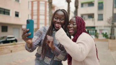 İki Afro-Amerikalı kadın parkta video görüşmesi yaparken gülümsüyor.