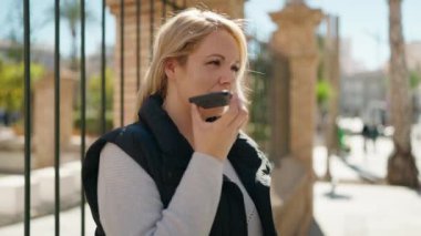 Genç sarışın kadın gülümsüyor. Kendine güveni tam. Akıllı telefondan konuşuyor.