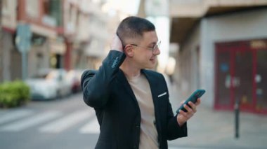 Young hispanic man executive smiling confident using smartphone at street