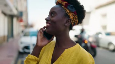 Genç Afrikalı Amerikalı kadın gülümsüyor. Kendine güveni tam. Sokakta akıllı telefondan konuşuyor.
