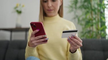 Genç sarışın kadın akıllı telefon ve kredi kartıyla alışveriş yapıyor.
