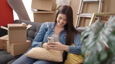 Young beautiful hispanic woman smiling confident using smartphone at new home