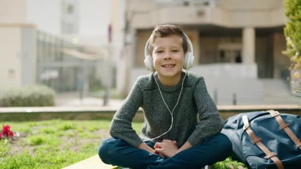 Ξανθό Παιδί Που Ακούει Μουσική Κάθεται Στο Γρασίδι Στο Πάρκο — Αρχείο Βίντεο