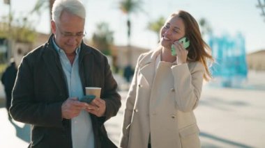 Orta yaşlı çift akıllı telefon kullanıyor ve parkta kahve içiyor.