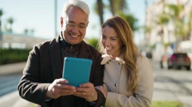 Orta yaşlı çift parkta video görüşmesi yaparken gülümsüyor.