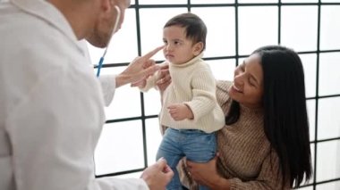 Çift ve oğul klinikte steteskopla bebeği muayene ediyor.