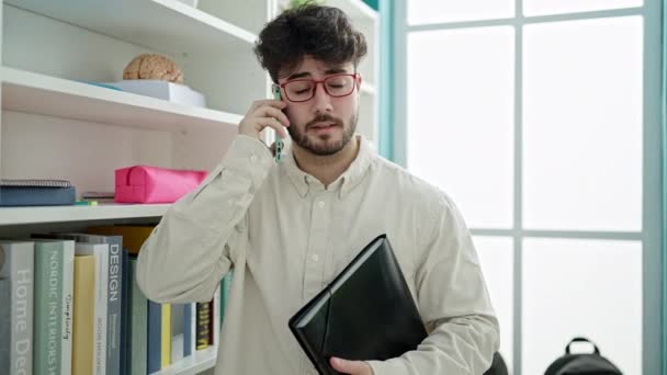 Jovem Hispânico Homem Estudante Segurando Binder Falando Smartphone Universidade Biblioteca — Vídeo de Stock