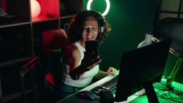 中年女性ストリーマー笑顔自信を持って作る自画によってスマートフォンでゲームルーム — ストック動画