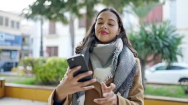 Genç, güzel, İspanyol bir kadın gülümsüyor. Parktaki akıllı telefonun yanında özçekim yapıyor.