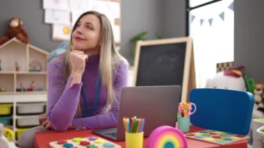 Anaokulunda dizüstü bilgisayar kullanan genç sarışın kadın anaokulu öğretmeni.