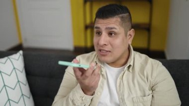 Genç İspanyol adam evdeki kanepede oturan akıllı telefonuyla sesli mesaj yolluyor.