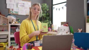 Young blonde woman preschool teacher teaching vocabulary lesson on video call at kindergarten