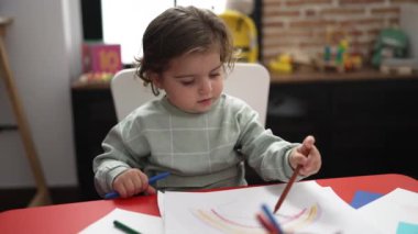 Anaokulunda masaya oturmuş kağıda resim çizen sevimli İspanyol kız öğrenci.