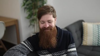 Young redhead man using smartphone sitting on sofa at home