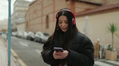 Genç İspanyol kadın sokakta akıllı telefon kullanarak müzik dinliyor.