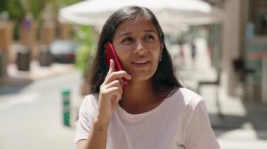 Genç, güzel, İspanyol bir kadın gülümsüyor ve caddede akıllı telefondan konuşuyor. 