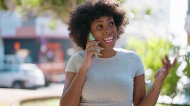 Genç Afrikalı Amerikalı kadın gülümsüyor. Kendine güveni tam. Sokakta akıllı telefondan konuşuyor.