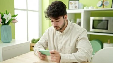 Yemek odasındaki kanepede oturmuş video oyunu oynayan İspanyol genç adam.