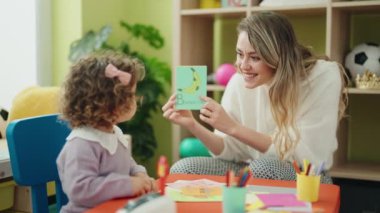 Teacher and toddler sitting on table having language lesson at kindergarten