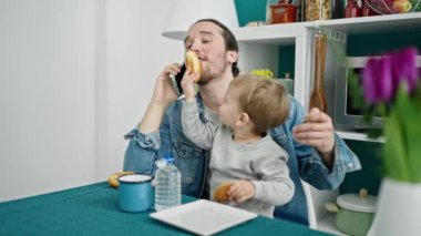 Baba ve oğul yemek odasında akıllı telefondan kahvaltı yapıyorlar.