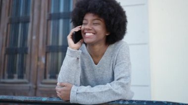 Afro-Amerikalı kadın gülümsüyor. Akıllı telefondan konuşuyor.